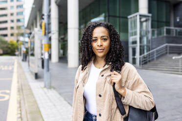 Confident woman with curly hair standing on footpath - WPEF06761