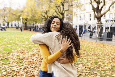 Lächelnde Frau mit geschlossenen Augen umarmt Freund im Herbst Park - WPEF06793