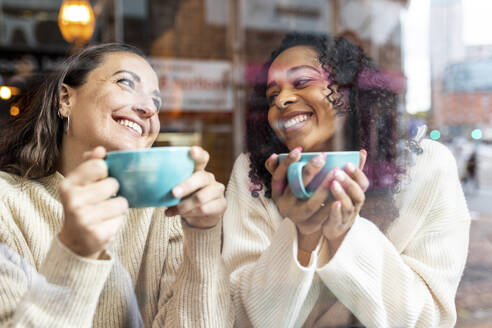 Glückliche Frauen genießen Kaffee im Café durch Glas gesehen - WPEF06809