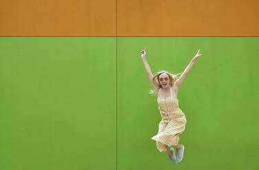 Fröhliche Frau, die vor einer grünen Wand springt - AZF00485