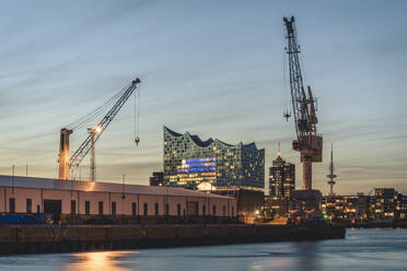 Germany, Hamburg, Harbor cranes at dusk with Elbphilharmonie in background - KEBF02481