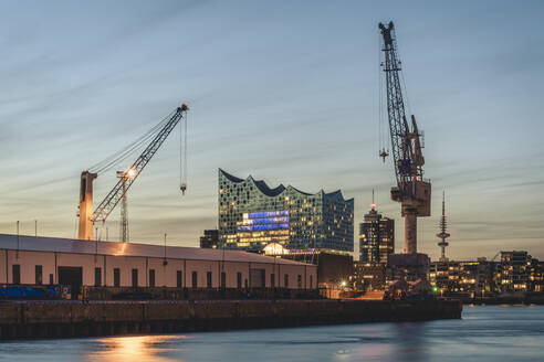 Deutschland, Hamburg, Hafenkräne in der Abenddämmerung mit Elbphilharmonie im Hintergrund - KEBF02481