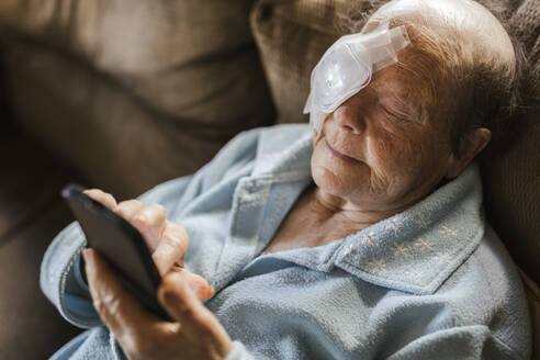 Injured senior woman using smart phone on sofa at home - LJF02309