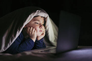 Junge kurz vor dem Einschlafen mit Laptop im Schlafzimmer - LJF02323