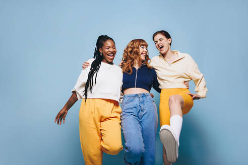 Eine Gruppe von fröhlichen Freundinnen, die sich umarmen und Spaß haben. Drei glückliche junge Frauen, die lachen und sich amüsieren, während sie vor einem Studiohintergrund stehen. - JLPSF28348