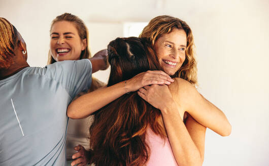 Eine Gruppe glücklicher Menschen, die sich lächelnd in einem Yogastudio umarmen. Fröhliche Menschen, die sich nach einer Yogastunde verabschieden. - JLPSF28441