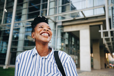 Young ambitious black woman smiling happily on her way to work in the morning. Young business woman looking away with excitement while commuting to the office in the city. - JLPSF28517