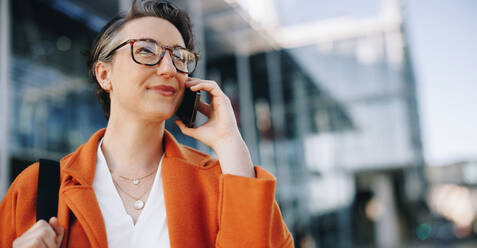 Geschäftsfrau beim Telefonieren auf dem Weg zur Arbeit in der Stadt. Reife Geschäftsfrau bei der Planung von Plänen für den Tag, während sie morgens zu ihrem Büro geht. - JLPSF28530