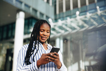 Cheerful young businesswoman using a smartphone during her morning commute in the city. Happy young business woman sending a text message on her way to the office. - JLPSF28533