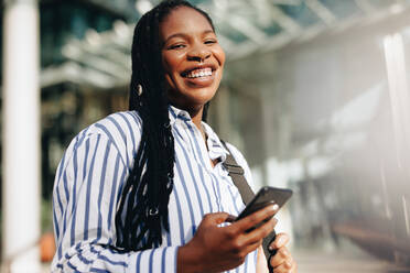 Portrait of a young black businesswoman smiling at the camera on her way to work in the city. Happy young business woman using a smartphone while commuting in the morning. - JLPSF28536