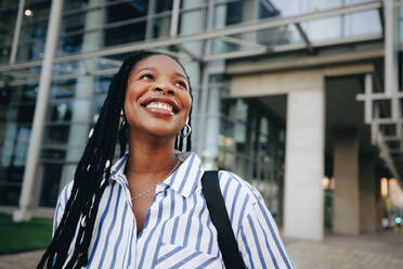 Aspiring young businesswoman smiling and looking away while commuting in the city. Happy young business woman listening to music on her way to the office in the morning. - JLPSF28555