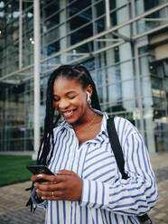 Happy young business woman smiling while looking at her smartphone during her work commute in the city. Cheerful young businesswoman playing music on her way to the office in the morning. - JLPSF28556