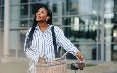 Aspiring young woman dreaming about her success while commuting with a bicycle in the city. Pensive young business woman traveling to work in the city. - JLPSF28561