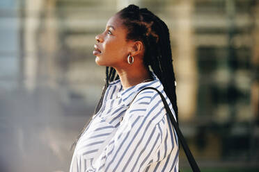 Sideview of a young businesswoman looking thoughtful while standing outdoors in the city. Young black business woman commuting to work in the morning. - JLPSF28566