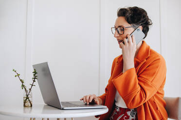 Reife Geschäftsfrau, die mit einem Laptop telefoniert, während sie in einem Café arbeitet. Geschäftsfrau, die ein Telefongespräch mit einem Kunden führt, während sie aus der Ferne arbeitet. - JLPSF28577
