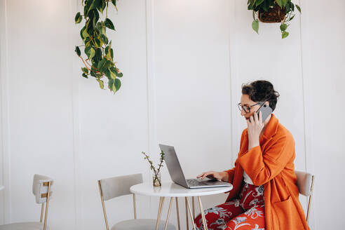 Reife Geschäftsfrau telefoniert und tippt auf einem Laptop, während sie in einem Café arbeitet. Reife Geschäftsfrau nimmt Kontakt mit einem Kunden auf, während sie aus der Ferne arbeitet. - JLPSF28578