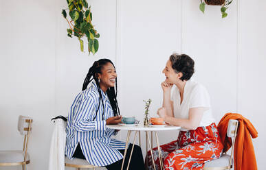 Zwei fröhliche Geschäftsfrauen, die während einer Kaffeepause in einem Café miteinander plaudern und lachen. Fröhliche Geschäftskolleginnen, die sich in einem Café freundlich unterhalten. - JLPSF28586