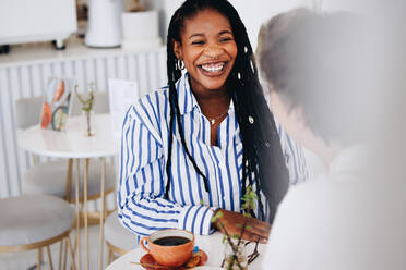 Fröhliche junge Geschäftsfrau, die während einer Kaffeebesprechung mit einem Kollegen in einem Café fröhlich lächelt. Zwei Geschäftsfrauen, die sich in einem modernen Café freundlich unterhalten. - JLPSF28589