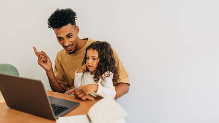 Junger Vater, der mit seiner Tochter zu Hause ein Lehrvideo anschaut. Liebevoller alleinerziehender Vater, der sein kleines Mädchen zu Hause mit einem Laptop unterrichtet. Vater und Tochter, die einen Online-Kurs besuchen. - JLPSF28624