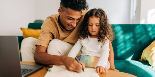Loving single father teaching his daughter how to draw with a colour pencil. Single dad homeschooling his young daughter. Father spending some quality time with his daughter at home. - JLPSF28630