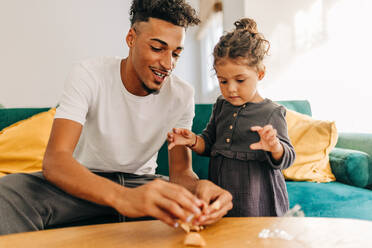 Glücklicher Vater und Tochter, die zu Hause einen Glückskeks öffnen. Verspielter alleinerziehender Vater, der sich mit seiner Tochter im Wohnzimmer amüsiert. Vater und Tochter verbringen eine schöne Zeit miteinander. - JLPSF28646