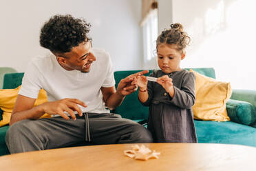 Playful young father laughing cheerfully while opening a fortune cookie with his daughter. Happy single father having fun while spending some time with his daughter at home. - JLPSF28647