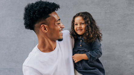 Adorable father and daughter laughing and having fun against a grey background. Happy single dad celebrating father's day with his young daughter. Father and daughter bonding. - JLPSF28656