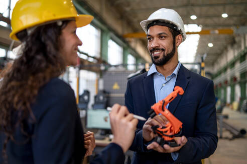 Ein Ingenieur hält ein Modell eines Industrieroboterarms und zeigt es einem Kollegen in einer Fabrik. - HPIF00701