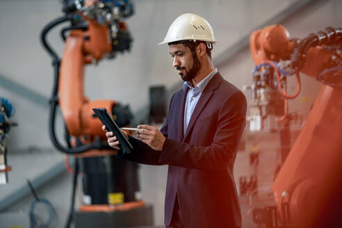 Ein Automatisierungsingenieur verwendet ein Tablet zur Programmierung eines Roboterarms in einer Fabrik. - HPIF00704