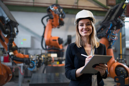 Eine weibliche Chefingenieurin in einer modernen industriellen Fabrik, die ein Tablet benutzt und eine Prüfung durchführt, aus einem langen Blickwinkel. - HPIF00713
