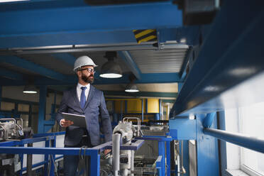 A chief Engineer in the hard hat walks through industrial factory while holding tablet. - HPIF00756