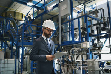 A chief Engineer in the hard hat walks through industrial factory while holding tablet. - HPIF00760