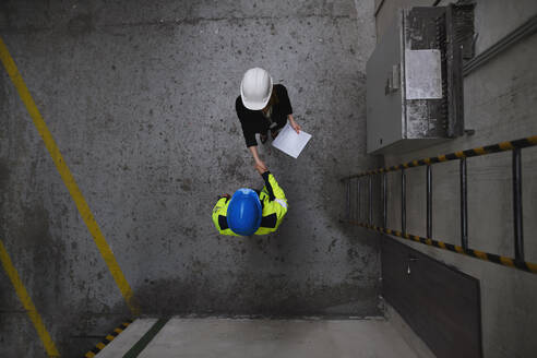 A top view of engineer and industrial worker in uniform shaking hands in large metal factory hall and talking. - HPIF00766