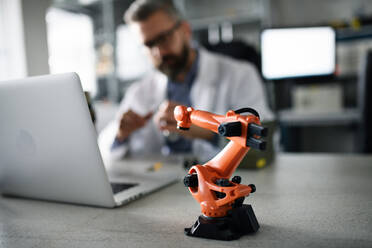 A robot arm industrial miniature figure on table in front of engineer working on laptop in laboratory. - HPIF00775