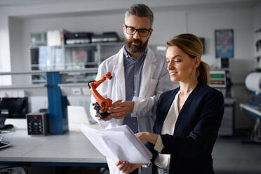 Robotics engineers with blueprints dicussing and desinging a modern robotic arm in laboratory. - HPIF00784