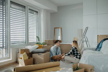 A cheerful young couple in their new apartment, sitting on floor and hugging. Conception of moving. - HPIF00790