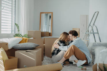 A cheerful young couple in their new apartment, sitting on floor and hugging. Conception of moving. - HPIF00794