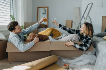 A cheerful young couple in their new apartment, sitting in boxes and clinking glasses. Conception of moving. - HPIF00802
