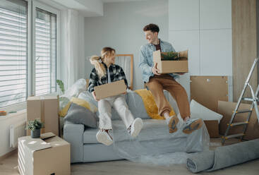 A cheerful young couple in their new apartment, carrying boxes. Conception of moving. - HPIF00806
