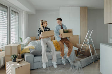 A cheerful young couple in their new apartment, carrying boxes. Conception of moving. - HPIF00807