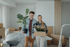 Ein fröhliches junges Paar in seiner neuen Wohnung, das Umzugskartons schleppt. Konzept des Umzugs. - HPIF00808