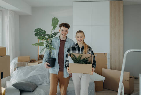 A cheerful young couple in their new apartment, carrying boxes. Conception of moving. - HPIF00808