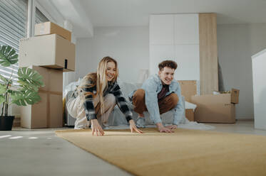 A cheerful young couple in their new apartment, rolling out carpet. Conception of moving. - HPIF00816