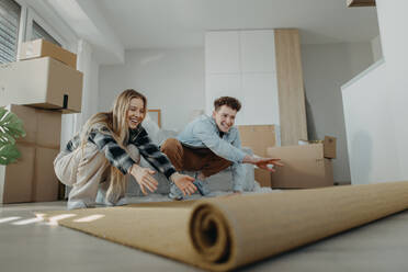 A cheerful young couple in their new apartment, rolling out carpet. Conception of moving. - HPIF00817