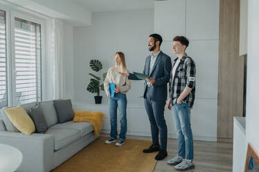 Ein glückliches junges Paar, das sein neues Haus kauft und einen Immobilienmakler in der Wohnung trifft. - HPIF00821
