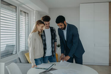 Ein junges Paar unterschreibt den Kaufvertrag für sein neues Haus und erhält die Schlüssel vom Immobilienmakler. - HPIF00826