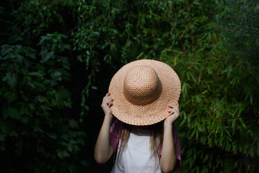 Ein unerkennbares kleines Mädchen mit Hut steht auf einem Bauernhof im Freien. - HPIF00869