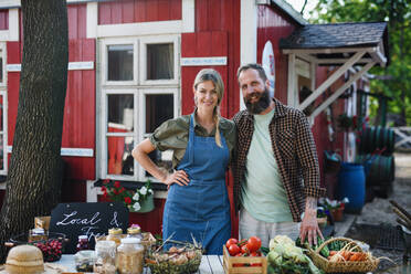 Ein älteres Landwirtepaar, das auf einem Bauernmarkt selbst angebaute Produkte verkauft, schaut in die Kamera. - HPIF00871