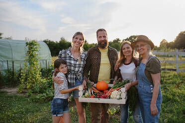 Eine glückliche Bauernfamilie schaut in die Kamera und hält ihre Ernte im Garten. - HPIF00882