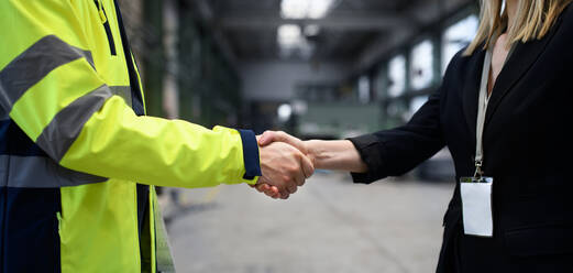Ein Ingenieur und ein Industriearbeiter in Uniform schütteln sich in einer großen Metallfabrikhalle die Hände und unterhalten sich, Nahaufnahme. - HPIF00918